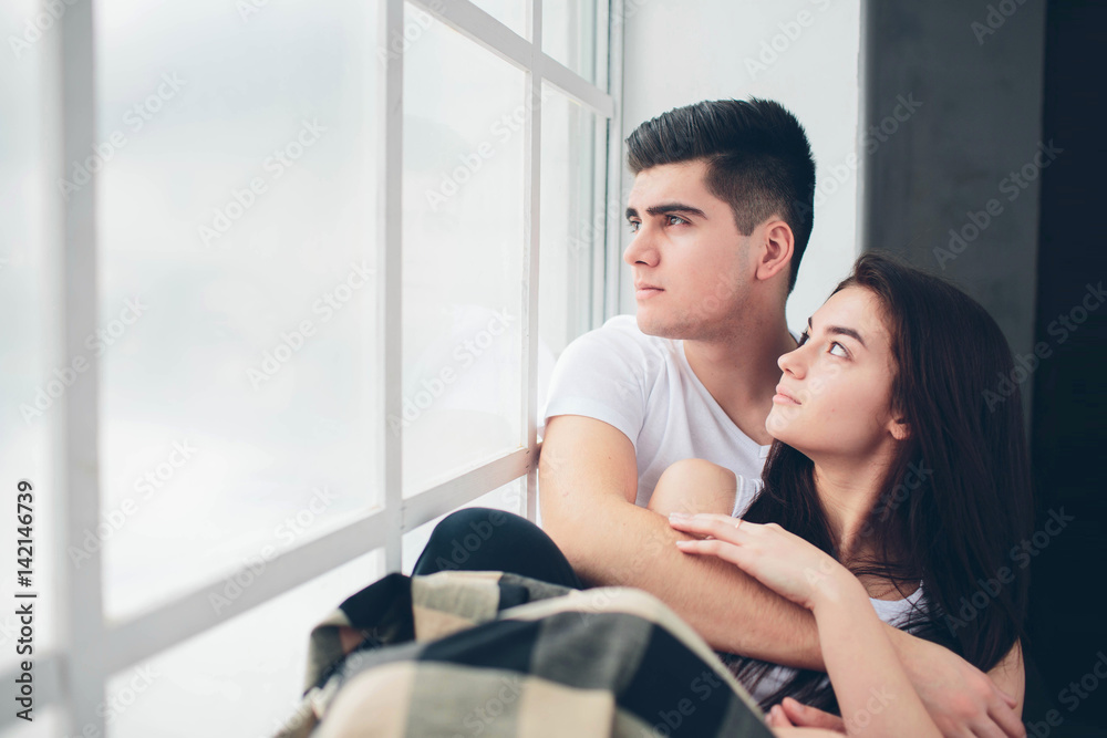 A loving couple are lying by a window bathed in sunlight. Bright and cozy bedroom. Family comfort and love A loving couple are lying by a window bathed in sunlight. Bright and cozy bedroom. Family comfort and love