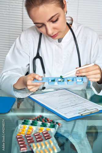 Physician or nurse in white coat selects pills for a patient checking his records