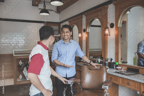 young barber expert smiling welcoming customer to his barbershop. please sit down