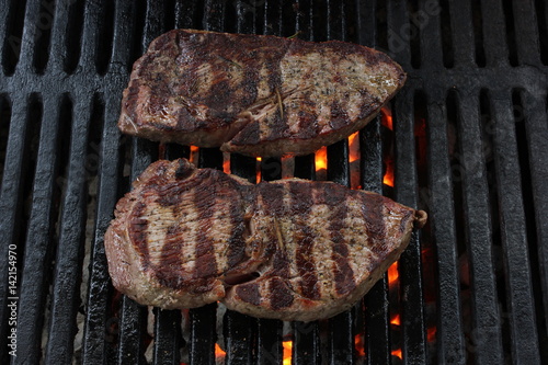 Two BBQ steaks on a charcoal grill with grill lines