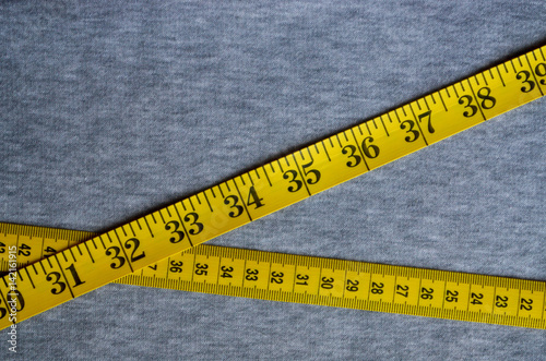 The Measuring Tape of Yellow Color with Numerical Indicators in the Form of  Centimeters or Inches Lies on a Gray Knitted Fabric. Stock Photo - Image of  sewing, ruler: 116542110