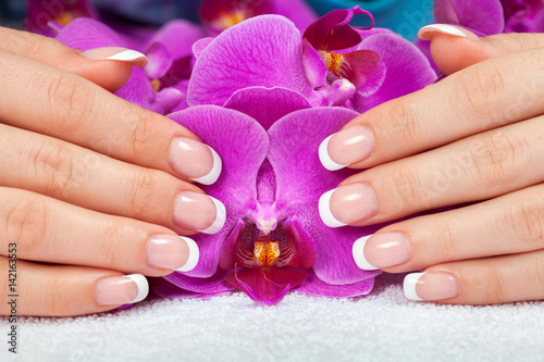 Beautiful female hands with french manicure on purple orchid flowers. Manicure salon.