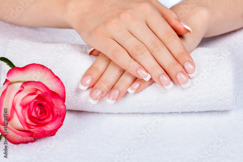 Beautiful female hands with french manicureon a white towel near rose flower. Manicure salon
