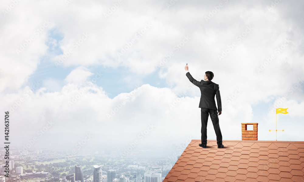 Businessman on house roof touch empty space. Mixed media