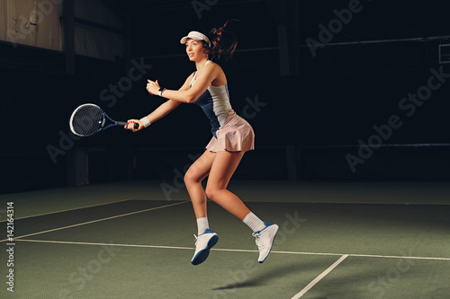 Female tennis player in action in a tennis court indoor.