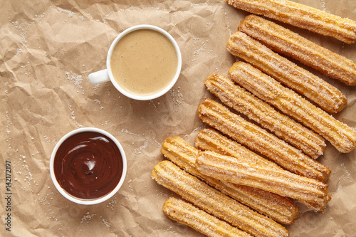 Churros traditional homemade Spain breakfast meal street food baked sweet dough dessert with cup of coffee and chocolate dipping on rustic decorative parchment paper background. Flat lay top view