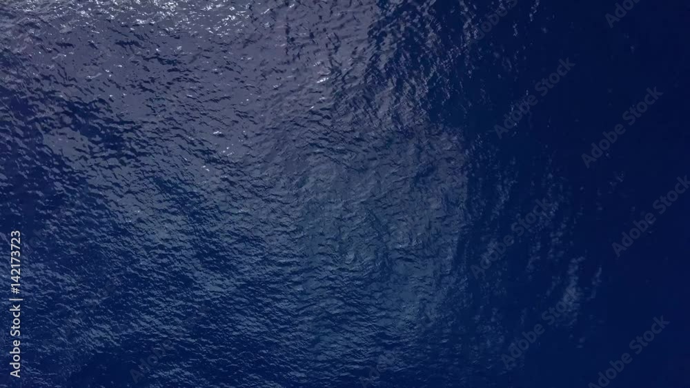 Top view of dark blue ocean water and tropical surface waves zooming out. Aerial drone shot over the sea