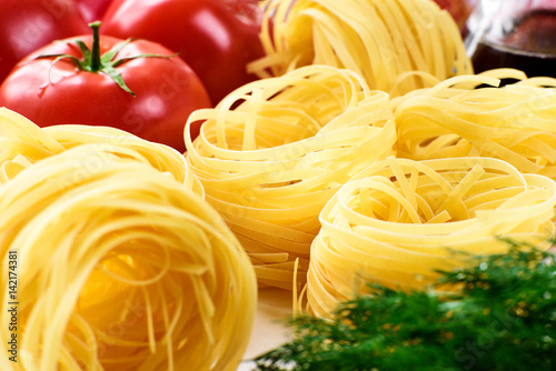 A close picture of red yellow and green contrasting goods products - pasta, tomatoes, greens.