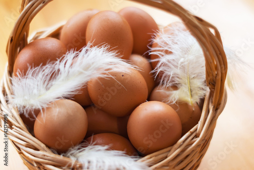 Closeup of a basket with organic chicken eggs and feathers. Defokus in the background. Eggs for easter. photo