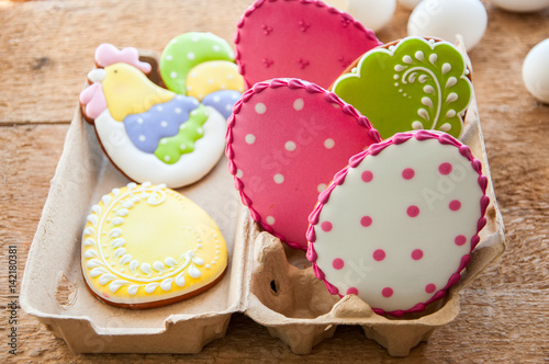 Tableau sur toile Close up of variety of colorful ester egg cookies with icing decoration in a craft paper container on a wooden background