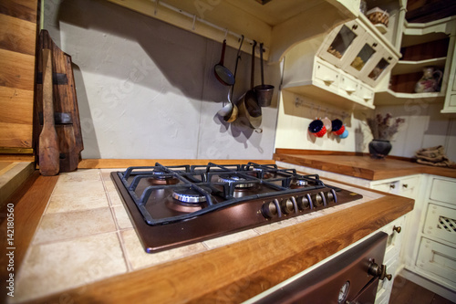 This is a big stove in a vintage kitchen. There are some ladles hanging on the wall. The kitchen is white.