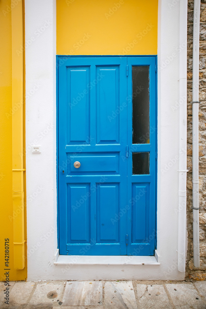 Dark blue old door with glass and forging on a yellow-and-white wall