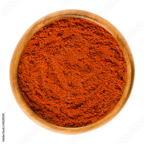 Sweet pepper red paprika powder in wooden bowl. Ground spice made from air-dried and smoked bell peppers, Capsicum annuum. Hungarian cuisine. Macro food photo close up from above on white background.