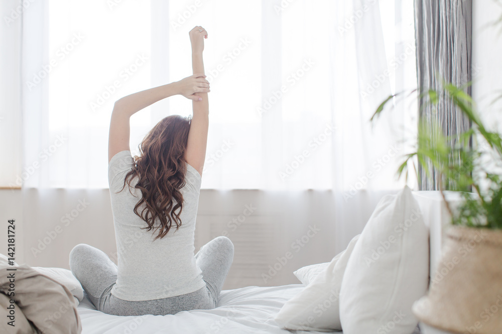 Female stretching sitting on bed in morning - obrazy, fototapety, plakaty 
