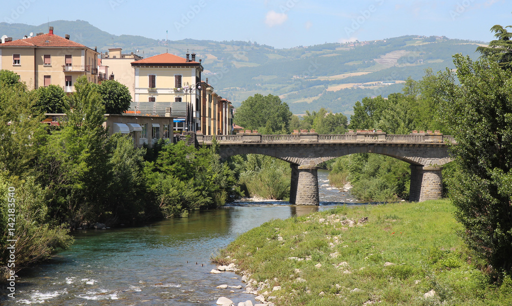 Houses and bridge across a small river in the background of mountains,Italy