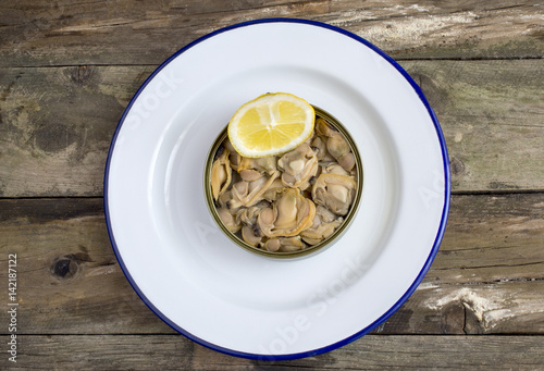 Can of preserved with clams on a plate on a rustic wooden table.
