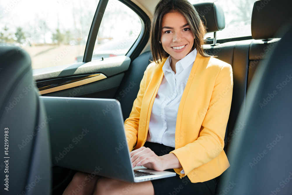 Portrait of a young businesswoman with laptop on back seat in car