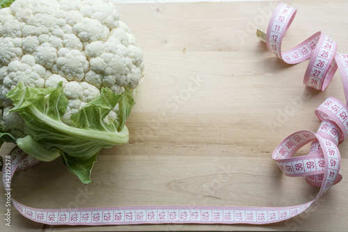 Fresh raw cauliflower with a tape measure on the wooden background
