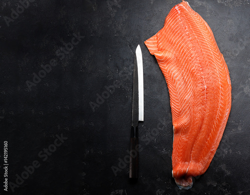 Fresh raw salmon fillet with chef knife over dark stone background