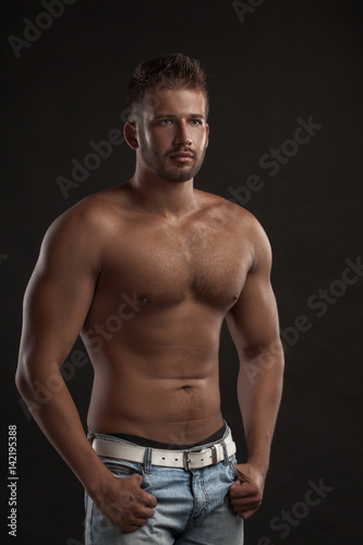 Model man with an open chested on a dark background , muscular body of a young man in jeans . Shot in a studio .