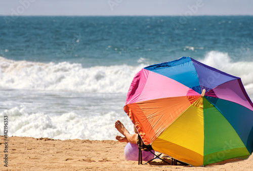 Tourist enjoying the beach under a colorful beach umbrella