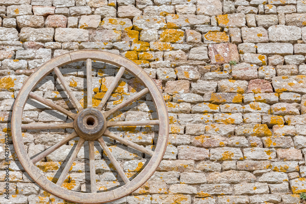  roue en bois appuyée contre un vieux mur de pierres 