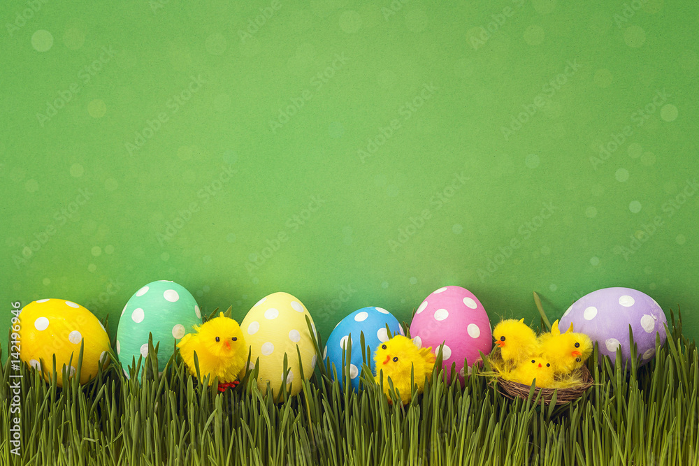 Easter eggs with decorative chicken in fresh grass on green background.