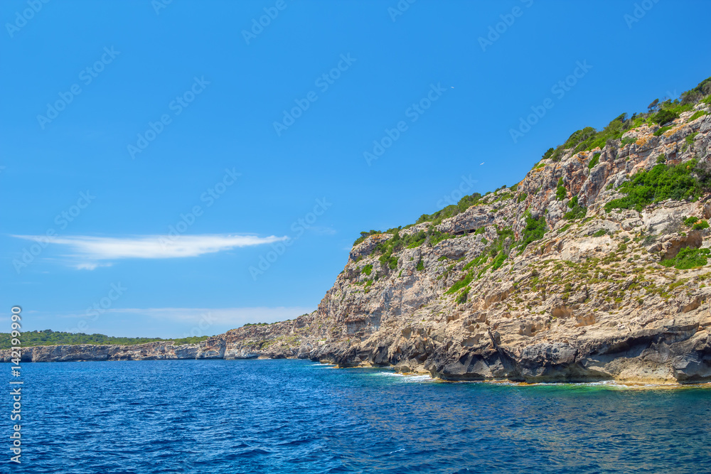 Menorca island coast with the cliffs covered with green bushes.