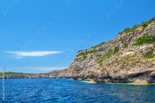 Menorca island coast with the cliffs covered with green bushes.