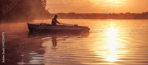 A young guy rides a boat on a lake during a golden sunset. Image of silhouette, Rower at sunset. Man rowing a boat in backlight of the sun