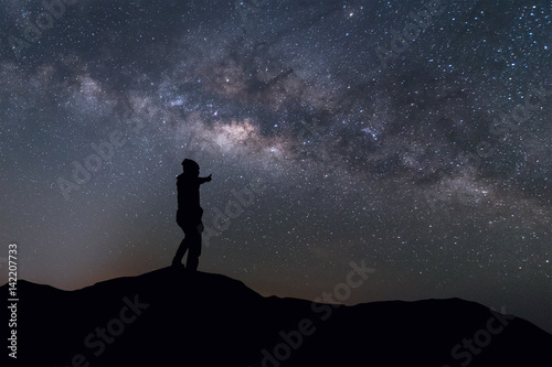Milky Way landscape. Silhouette man thump up and standing on top of mountain with night sky and bright star on background.