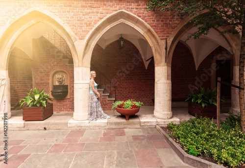 Beautiful young woman stands leaning on a column in an arched passage of the ancient university building in Krakow. Poland. Studying abroad. Student life. The ancient universities of Europe