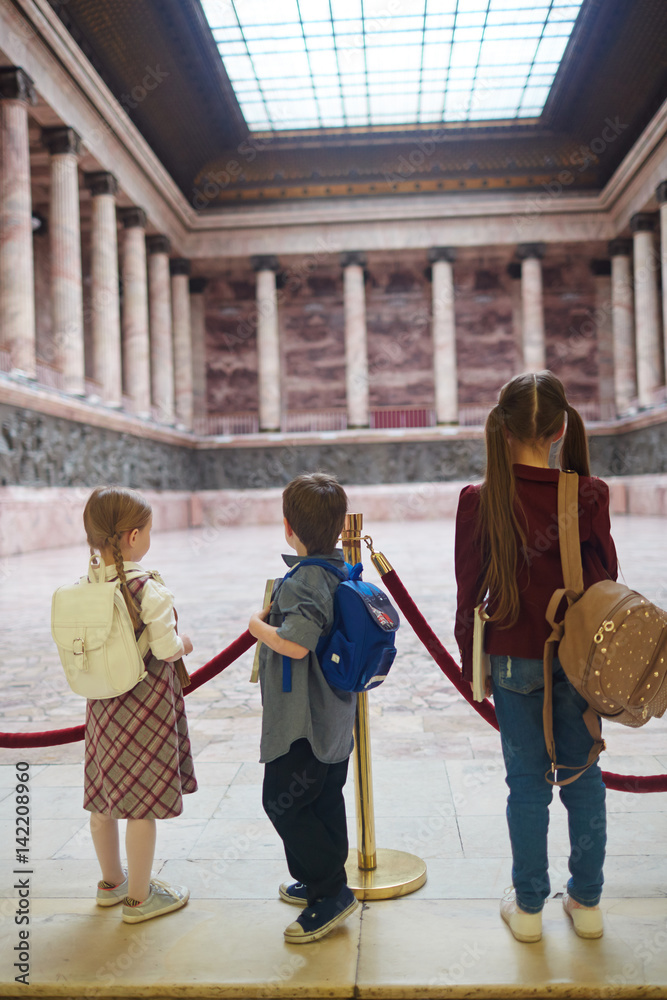 Three schoolkids with backpacks visiting modern museum