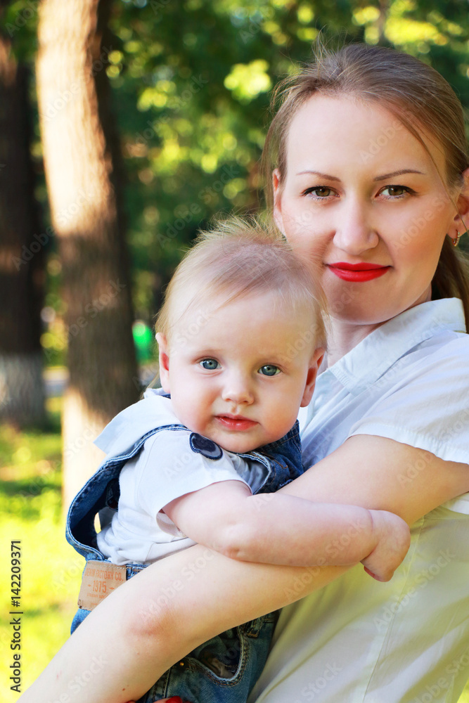 Happy family: mother and little baby son outdoor. Woman holding her child.  They looking in camera and smiling