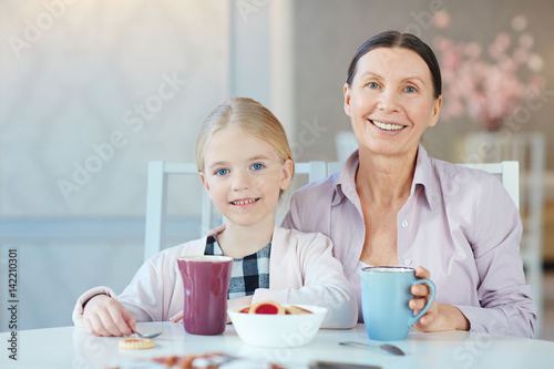 Senior female and her granddaughter having dessert or snack by table