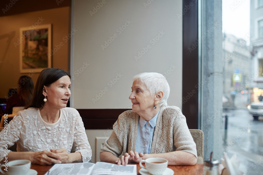 Two female buddies discussing article from magazine in cafe Two female buddies discussing article from magazine in cafe