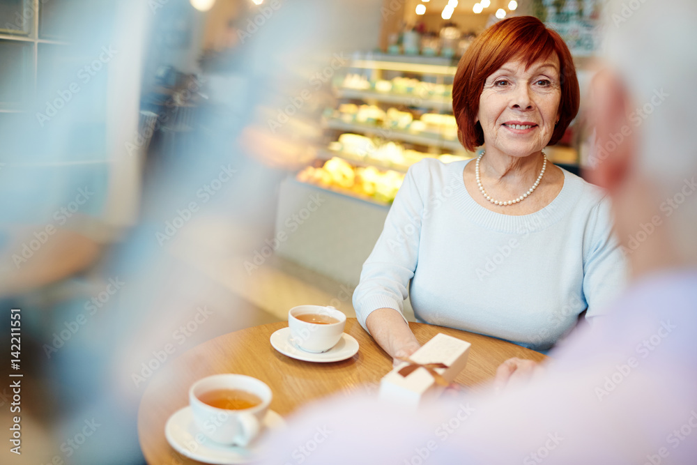 Aged woman with surprise in gift-box looking at her husband in cafe Aged woman with surprise in gift-box looking at her husband in cafe