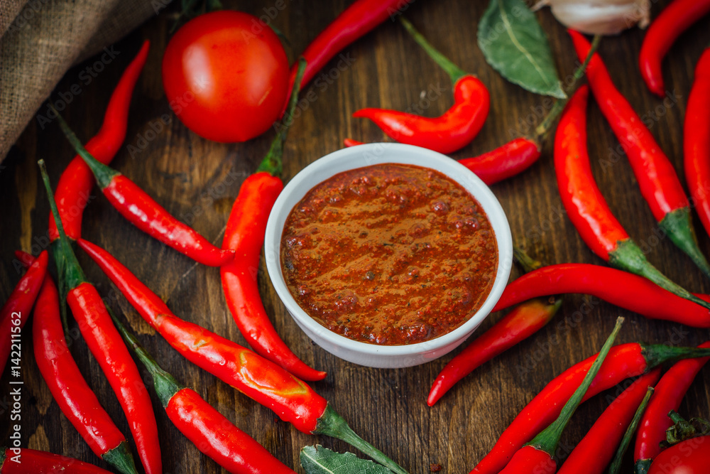 Red hot chili peppers and salsa or adjika in white ceramic bowl.