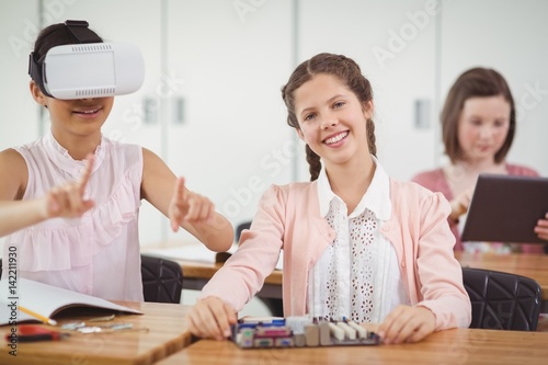 School girl sitting in classroom using virtual reality headset 