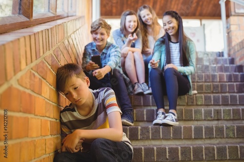 School friends bullying a sad boy in school corridor photo