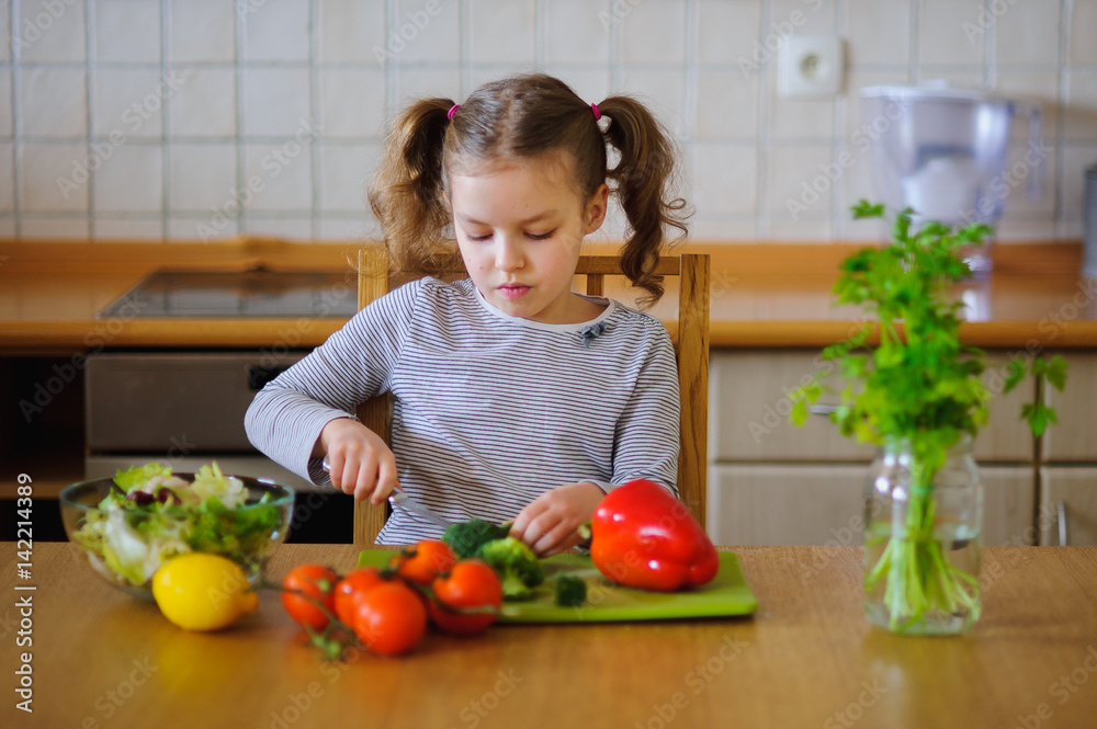 Cute girl of younger school age cuts vegetables and greens for salad. Cute girl of younger school age cuts vegetables and greens for salad.