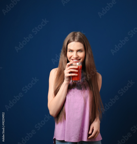 Beautiful young woman with glass of fresh juice on dark blue background