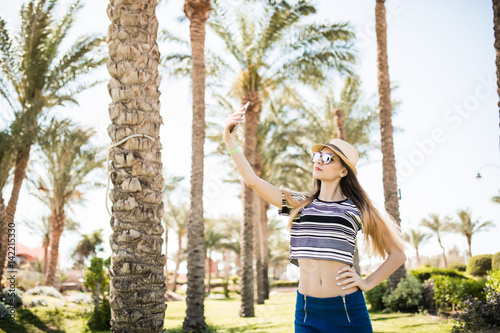 young woman taking selfie with smartphone on summer palms background. Summer vocation,