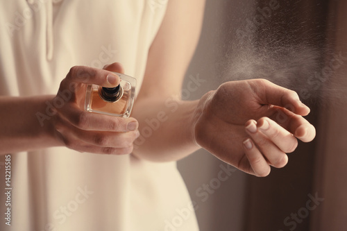Beautiful young woman with bottle of perfume at home, closeup photo