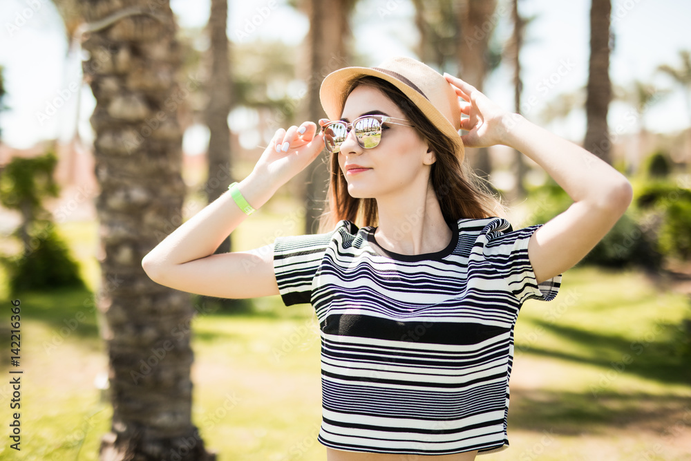 Cheerful young woman in hat and sunglasses in summer palms backgrounds. Summer vocation.