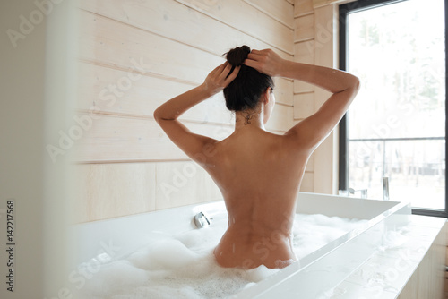 Young woman having bubble bath and looking at window
