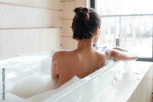 Murais de parede Young woman having bubble bath and looking at window