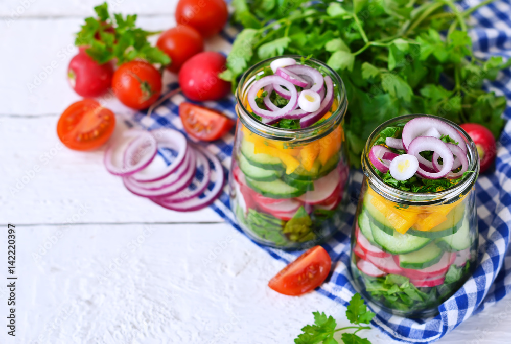 Vegetable salad with spinach and red onions in a glass jar on a white background