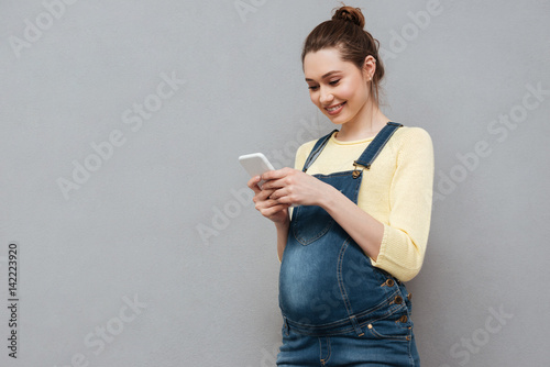 Portrait of a smiling cute pregnant woman using mobile phone photo