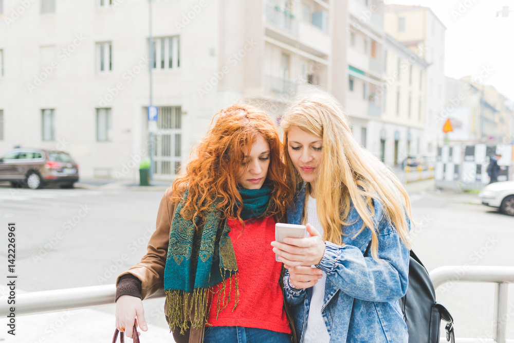 Two young women using smart phone outdoor  - technology, social network, communication concept